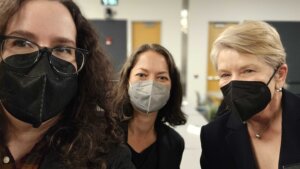 A picture of #MEAction Scientific Director, Jaime Seltzer (left), Katie Brennan (middle), and Dr. Sally Hodder (right). All three smile behind face masks.