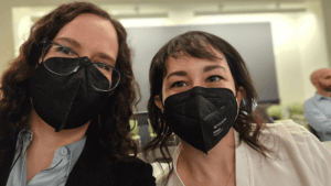 Jaime and Angela side by side in the conference room at NIH. Angela has darker hair and is wearing a cream top. Both are wearing black face masks