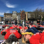 A group of people wearing red #MillionsMissing shirts lying down en masse at a demonstration in Scotland.