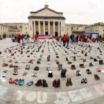 Rows of shoes representing the millions missing in front of a building in Southampton. Chalk lettering reads #CanYouSeeMeNow